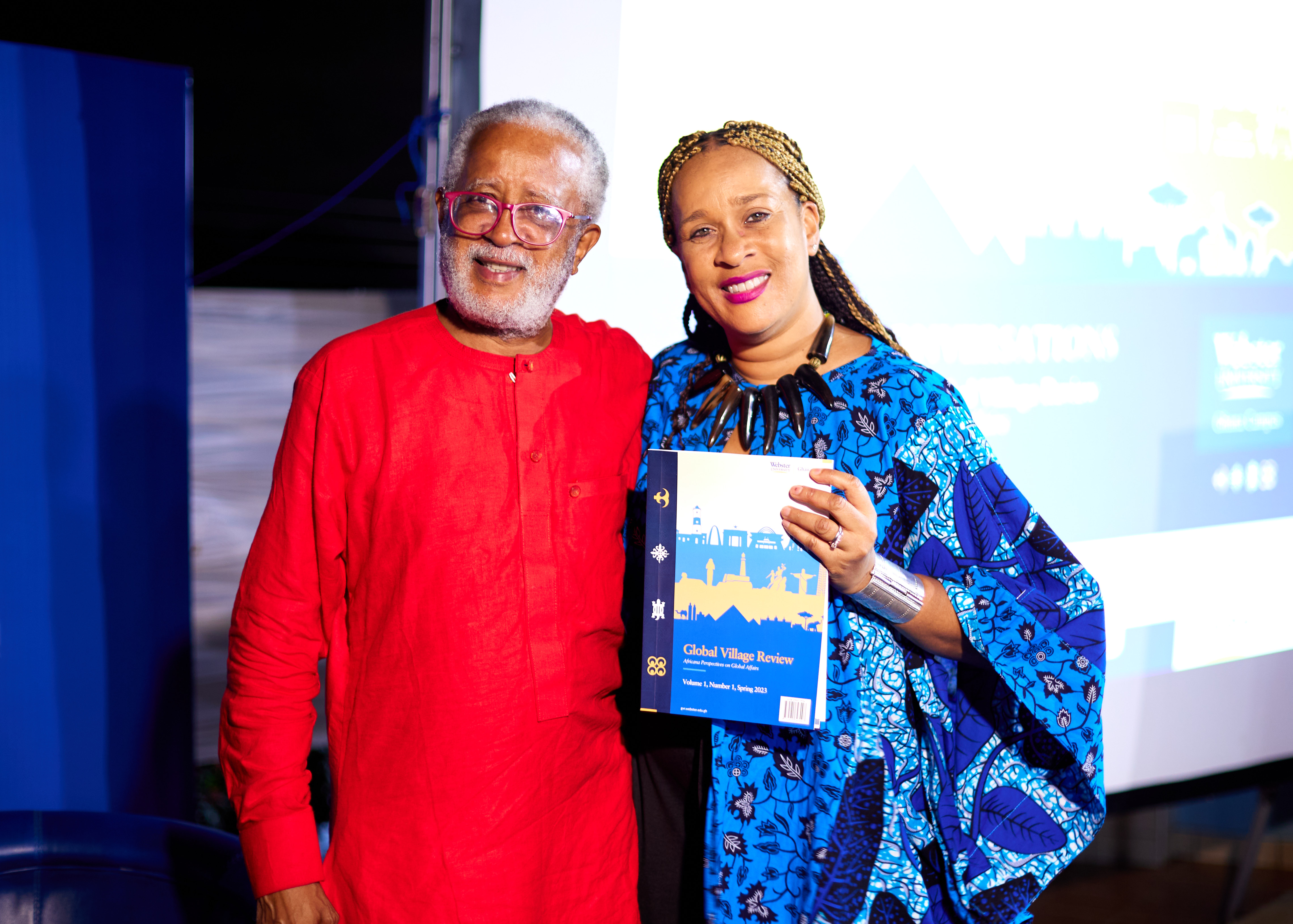 Williams and Sanders smille with a printed copy of the Global Village Review.