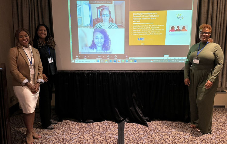 The group prepares to present in a conference room with their slideshow onscreen, along with two additional presenters on Zoom.