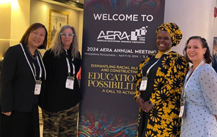 Four Webster University representatives stand next to the "Welcome to AERA" sign at the entrance to the conference.