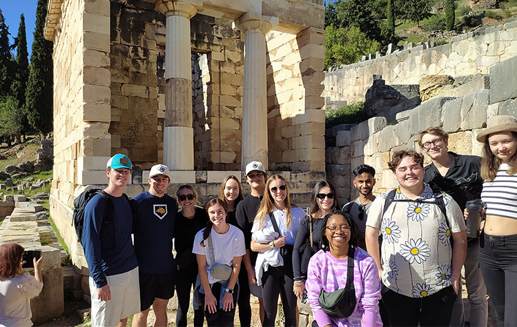 A group of students studying abroad in Athens stand in front of the ruins of the Treasury of Athens.