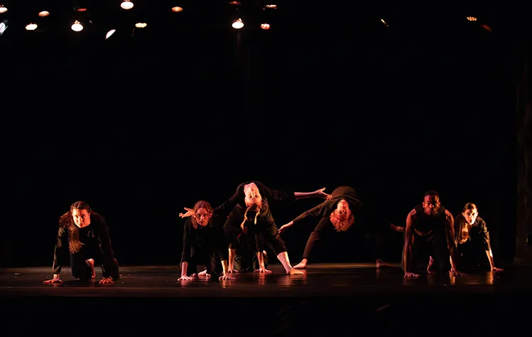  Webster University BFA Candidates perform onstage wearing dark colors in low lighting.