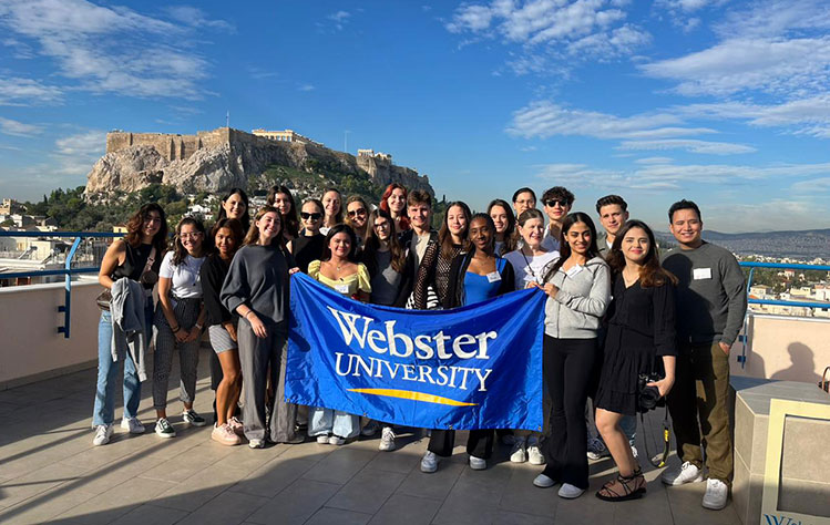 Webster LEADS students with a Webster banner on the rooftop of Webster Athens.