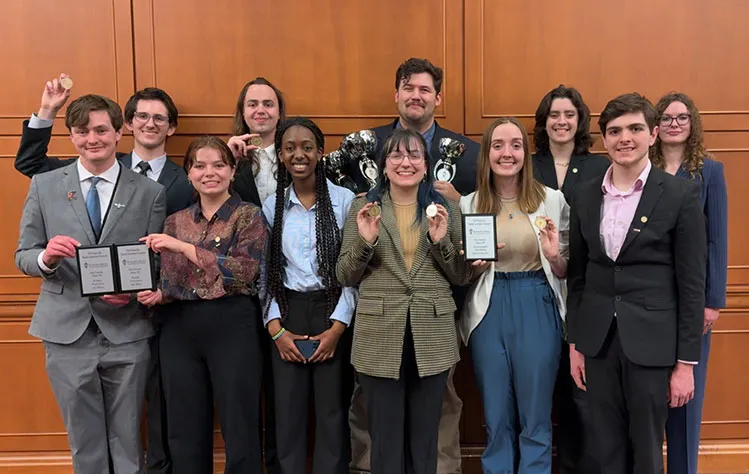 The Webster University Forensics and Debate team poses for a group photo with medals, trophies and plaques.
