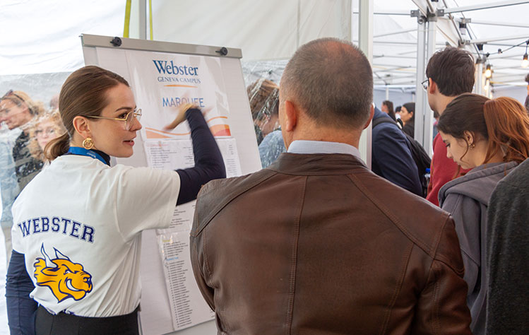 A woman in a Webster shirt points to a posterboard in a crowd.