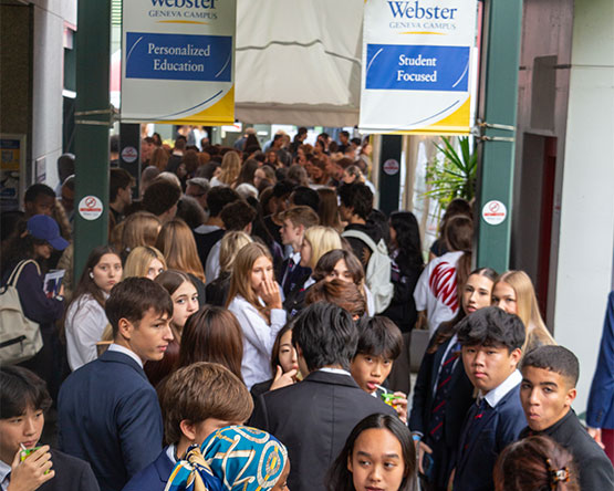 A crowd of people walk underneath Webster banners inside the Geneva campus.