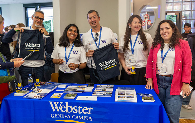 Five people wearing Webster shirts pose and smile behind a table at the event.