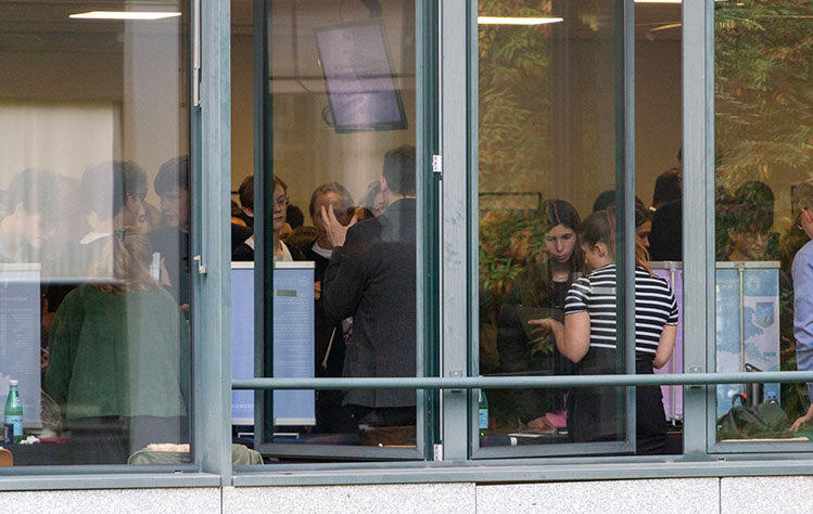 Through a window from the outside looking in, attendees are seen speaking to representatives at tables.