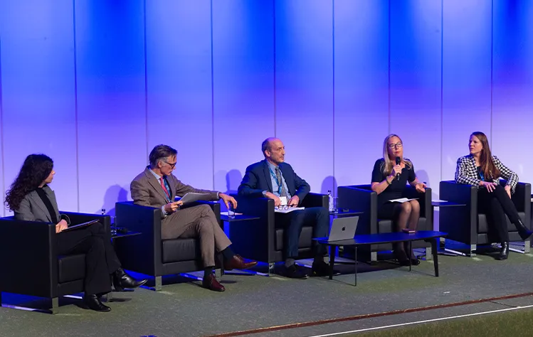 Panelists sit onstage with blue lighting in the background.