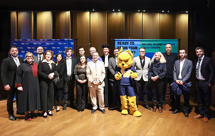 Webster University Georgia faculty pose for a photo with the Gorlok during the event in front of a Georgia step and repeat.