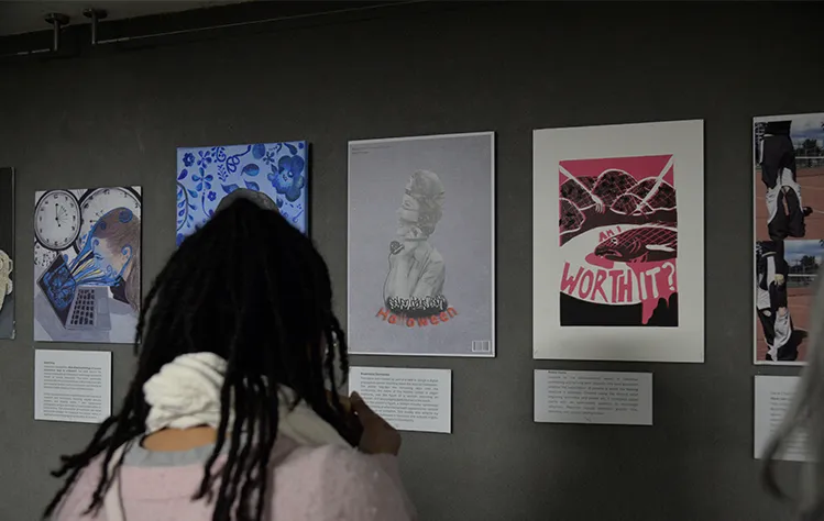 An event attendee views several student art pieces on a wall in the Gorlok Gallery with descriptions underneath.