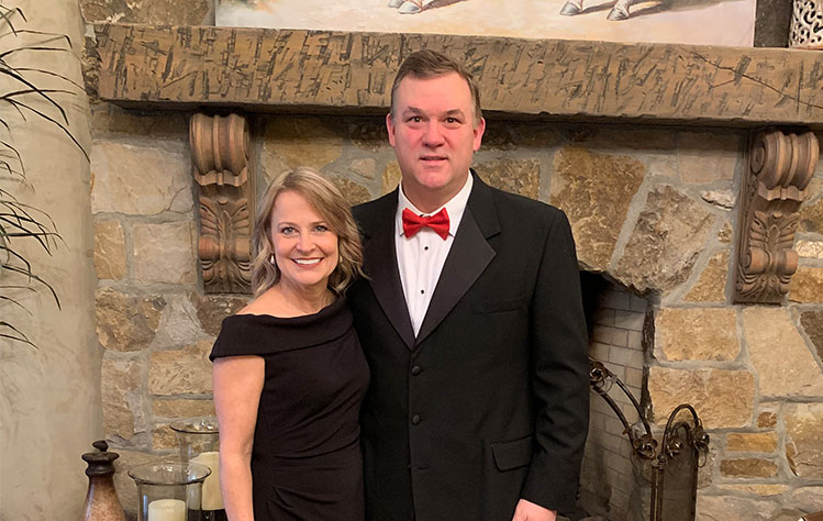 Kelly and Rand Harbert stand in front of a fireplace mantle.