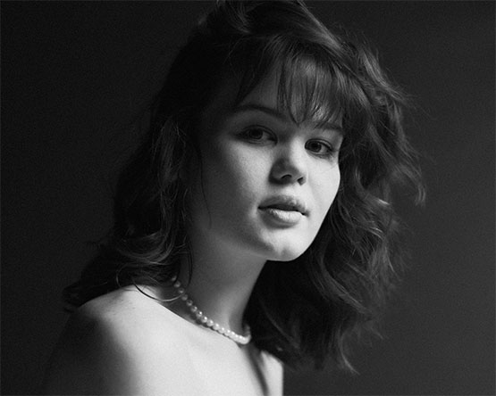 A black and white photograph of a woman with long hair and a pearl necklace..