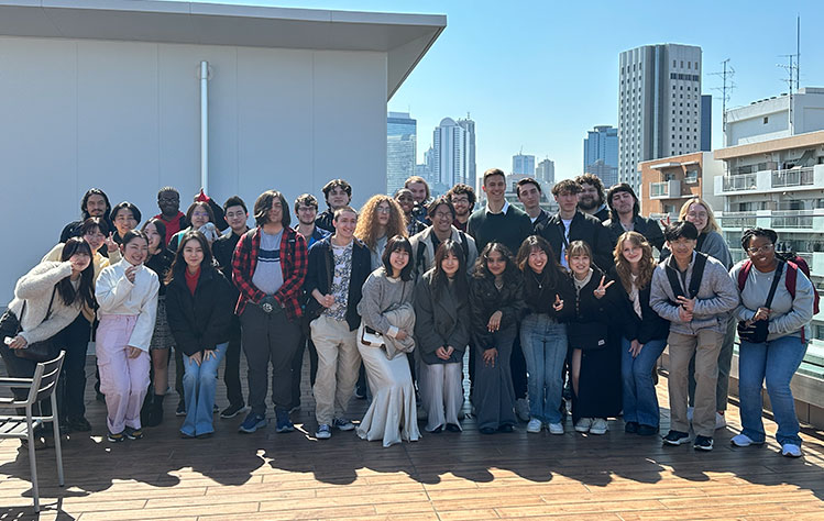 Students and Burton stand for a large group photo on the roof of a building on a sunny in Japan.