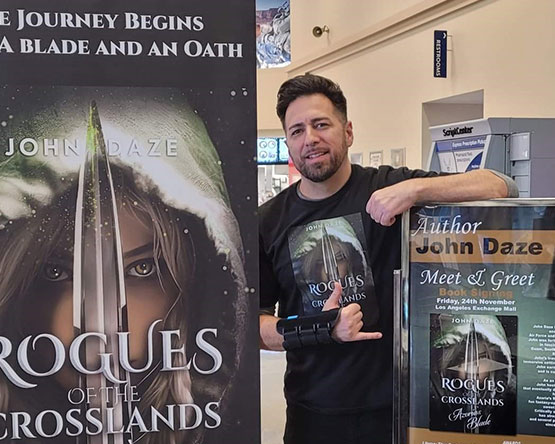 John Daze stands by a meet and greet poster and a banner advertising Azoria's Blade.