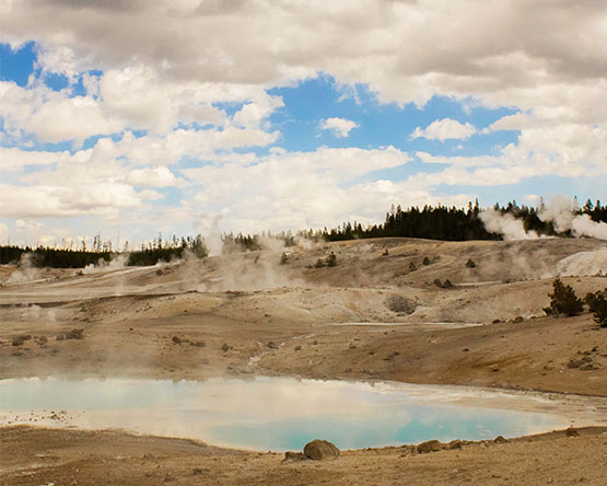 A scenic landscape of steaming hot springs and geysers, tans and blues.