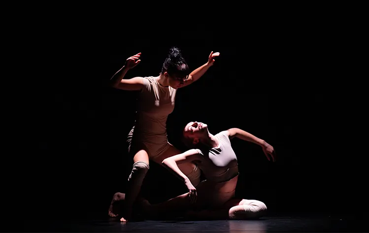 Junior Ally Lame (left) and freshman Alivia Fletcher dance onstage in low lighting.