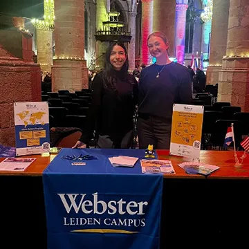 María Lindado and Nikki Jennings stand behind a table with Webster University Leiden materials inside the Pieterskerk.