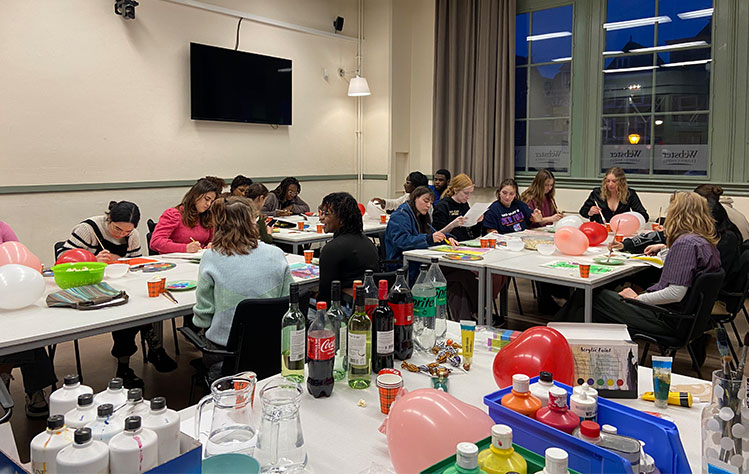 Event attendees sit in a classroom at Webster Leiden and paint during the event.