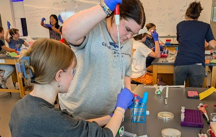 Two PHAGE camp participants use lab equipment while wearing safety goggles and gloves.