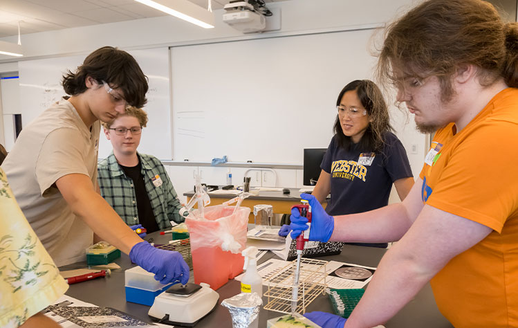 Mary Lai Preuss, department chair of Biology, looks on while camp attendees perform an experiment. 