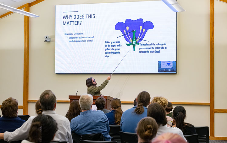 An Impact Center student points to cross-section of a flower on presentation slide