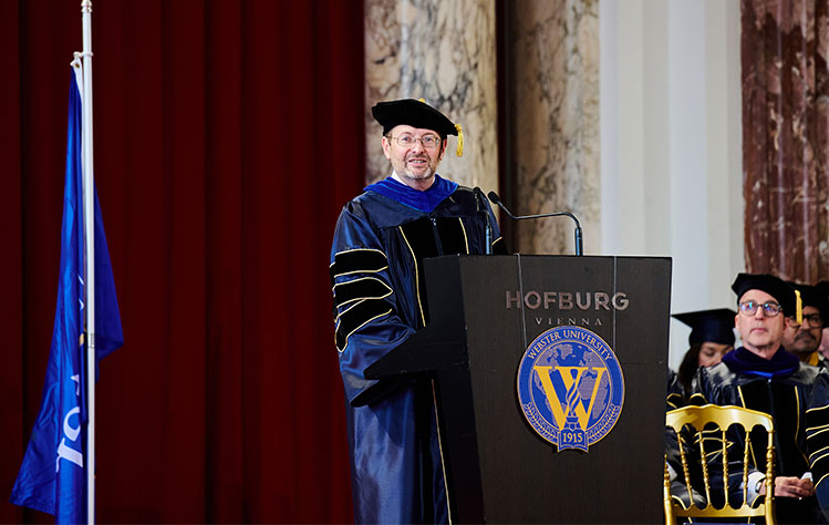 Rector Johannes Pollak stands at the commencement podium in regalia.