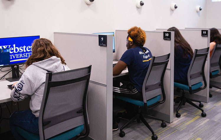 A row of students facing computers and between dividers at the testing center.