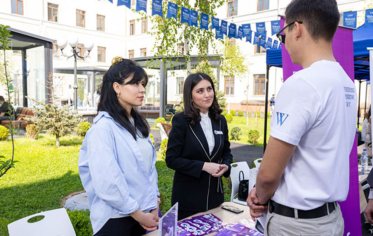 A Webster student wearing a Webster University collared shirt speaks with two company representatives at the Webster University Tashkent career fair.