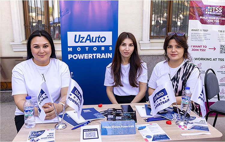 Three hiring representatives sit behind a blue and white table at the Webster University in Tashkent career fair.