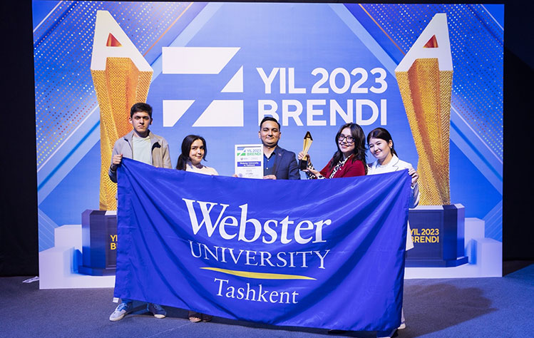 Five Webster Tashkent representatives hold the Brand of the Year plaque, trophy and a Webster University in Tashkent banner in front of the conference banner.