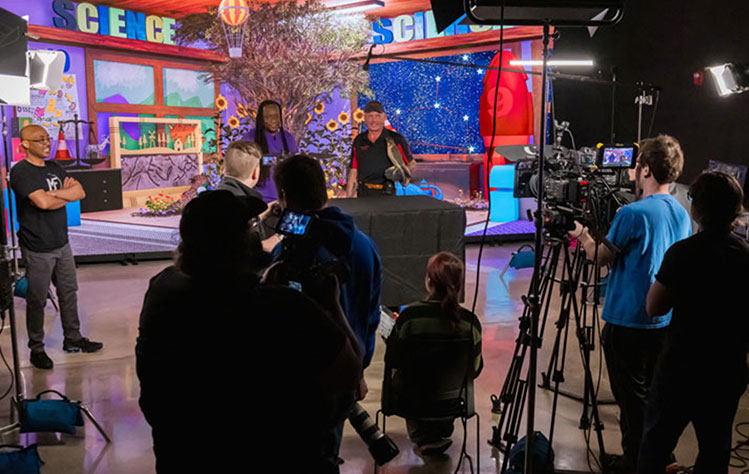 Webster students stand behind cameras while filming an episode of Teaching in Room Nine in front of the virtual cinematic wall in Webster's Sverdrup Complex, home to the School of Communications.