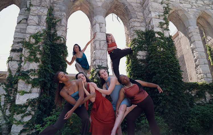Verdant dancers pose with stone arch background.