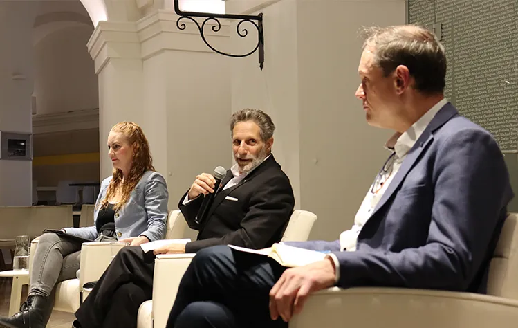 Erin K. Jenna, Samuel R. Schubert and Bradley Wiggins sit onstage with a microphone during the event.