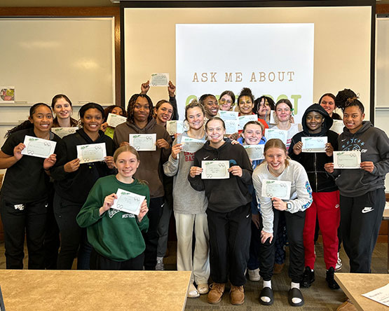 The 2023-24 Women’s Basketball Team poses for a group photo in a classroom while holding Green Dot Training Pledges.