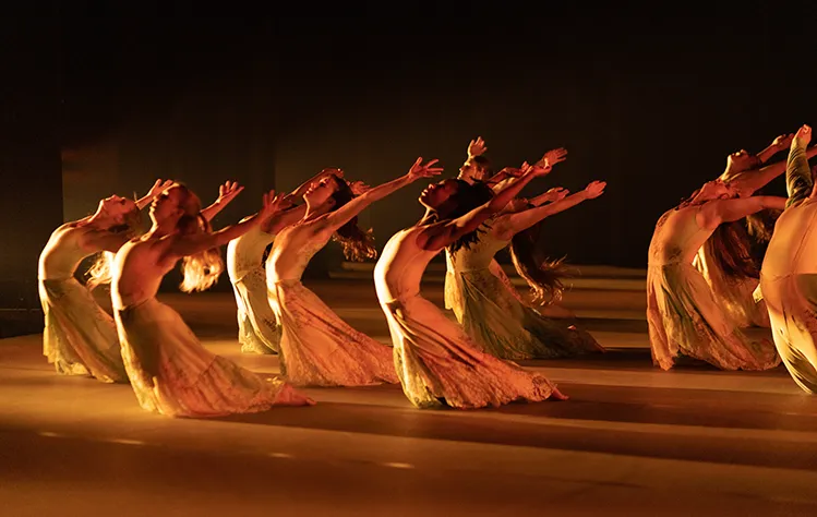 A group of female dancers on their knees with hands in the air. Photo by Gerry Love.